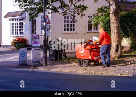 Postboten, die die Post mit dem Wagen-Trolley-High Street Henley in Arden Warwickshire England entlten Stockfoto