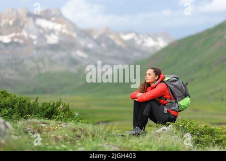 Wanderer in Rot sitzend und die Aussicht auf einen grünen Berg betrachtend Stockfoto