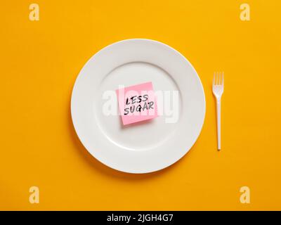 Notizbuch mit dem Wort weniger Zucker auf einem weißen Teller. Weniger Zuckeraufnahme und gesundes Ernährungskonzept. Stockfoto