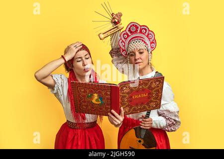 Musikerinnen in russischen Volkskleidern mit Musikinstrumenten auf gelbem Studiohintergrund - Moskau, Russland, 17. Juni 2022 Stockfoto