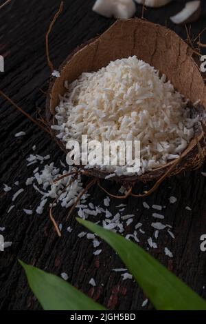 Gehackte Kokosnuss auf einem hölzernen Hintergrund, Draufsicht. Kokosmilch und Kokosflocken sind tropische Lebensmittel Stockfoto