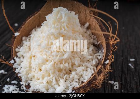 Gehackte Kokosnuss auf einem hölzernen Hintergrund, Draufsicht. Kokosmilch und Kokosflocken sind tropische Lebensmittel Stockfoto
