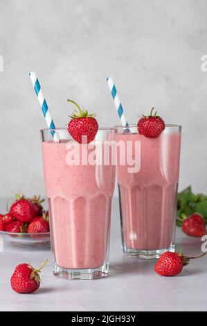 Hausgemachter Milchshake mit Erdbeeren in zwei Gläsern mit Trinkhalmen auf hellgrauem Hintergrund Stockfoto