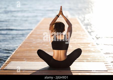 Rückansicht einer Frau in Sportkleidung, die am Strand meditiert Stockfoto