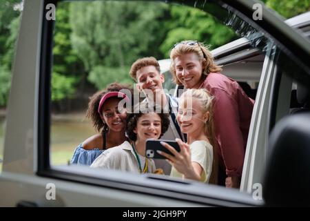 Multirassische junge Freunde, die zusammen mit dem Auto reisen, Selfie machen – Sommerferien, Urlaub, Reisen, Roadtrip und People-Konzept. Stockfoto