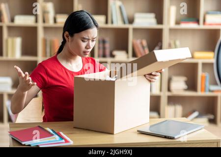 Frustriert enttäuscht junge japanische Dame öffnet Karton und traurig für Fehler mit Paket Stockfoto