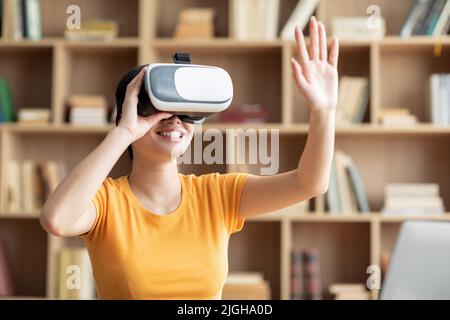 Lächelnd überrascht japanische Frau in vr Brille spielt im Online-Spiel und berührt leeren Raum mit der Hand Stockfoto