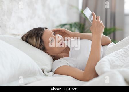 Unglückliche Frau, die ihr Smartphone benutzt und ihren Kopf berührt Stockfoto
