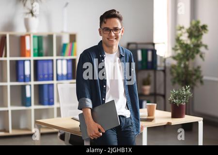 Modernes Unternehmertum. Millennial Businessman Holding Laptop Steht In Der Nähe Des Schreibtisches Im Büro Stockfoto