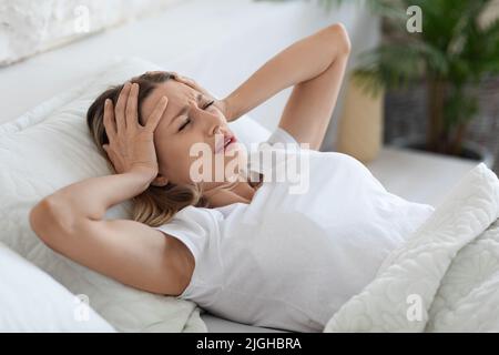 Gestresste Frau, die unter Kopfschmerzen leidet und ihren Kopf berührt Stockfoto