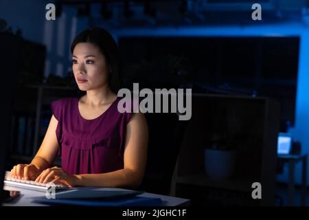 Fokussierte asiatische Geschäftsfrau, die nachts am Schreibtisch im Büro am Computer arbeitet Stockfoto