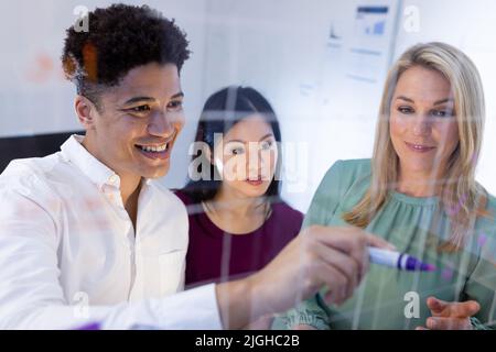 Lächelnde, multirassische Mitarbeiter diskutieren und Brainstorming über Glaswände in einem modernen Büro in der Nacht Stockfoto