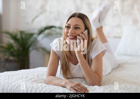 Glückliche, hübsche Dame, die im Bett telefoniert hat Stockfoto