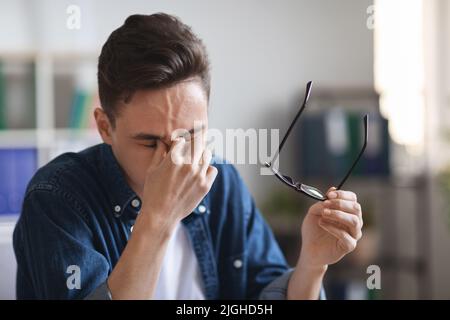 Porträt Eines Müden Jungen Mannes, Der Eine Brille Auszieht Und Sich An Der Nasenbrücke Reibt Stockfoto