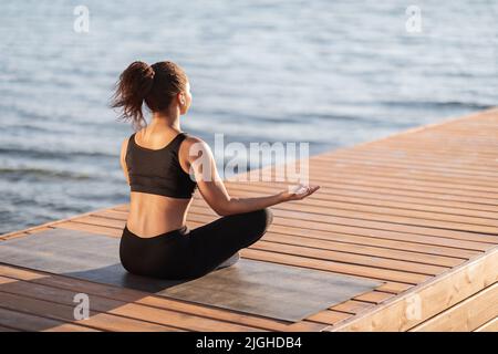 Nicht erkennbare afroamerikanische Frau, die durch Wasser meditiert Stockfoto