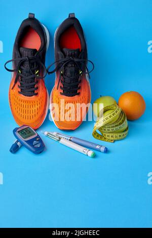 Orangefarbene Sneakers, Früchte, Maßband, Glucometer und Insulin-Spritzenstifte auf blauem Hintergrund. Bewegung, Ernährung und Diabetes-Management Stockfoto