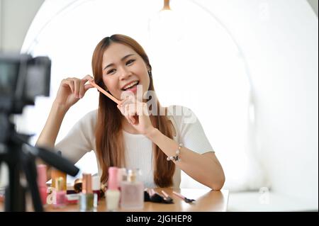 Schöne junge asiatische weibliche Beauty-Bloggerin zeigt Kosmetikprodukte einer Kamera und macht ein Make-up Tutorial Video für ihre Schönheit und Mode Blog. Stockfoto