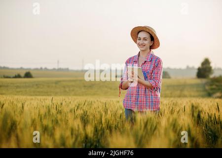 Ein junger Fcrmer überprüft ein Getreidefeld und sendet Daten von einer Tablette an die Wolke. Konzept von Smart Farming und digitaler Landwirtschaft. Erfolgreiche Produktion Stockfoto