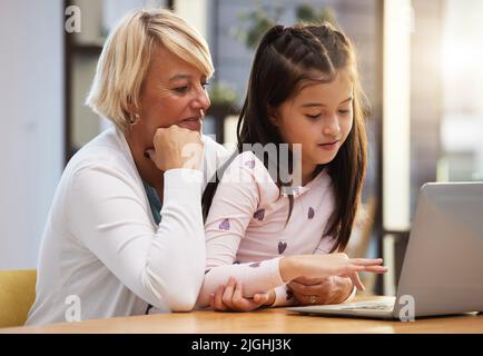 Ein kleines Mädchen mit einem Laptop, während sie mit ihrer Großmutter sitzt. Stockfoto