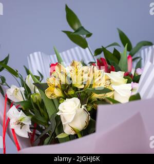 Nahaufnahme von hellen Strauß von farbigen Blumen in Geschenkpapier eingewickelt. Bouquet von gelben, roten und weißen Blumen mit Grün als Symbol des Kompliments Stockfoto