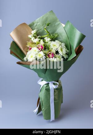 Originell schönes Bouquet mit weißen Chrysanthemen, Onoma, Iris und grünen Zweigen. Blumenstrauß eingewickelt in Kraft und grünem Papier mit Weiß Stockfoto