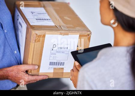Bestellungen und Lieferungen mit Technologie verfolgen. Aus dem Hochwinkel eine Aufnahme eines nicht erkennbaren Mannes, der ein Paket von einer Kurierin abgeliefert hat. Stockfoto