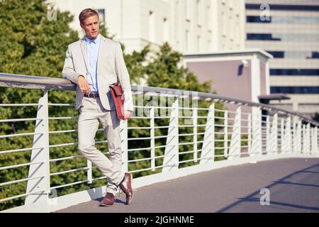 Überbrückung der Kluft zwischen Ehrgeiz und Erfolg. Die ganze Aufnahme eines hübschen jungen Geschäftsmannes, der am Morgen auf dem Weg zur Arbeit eine Brücke überquert Stockfoto