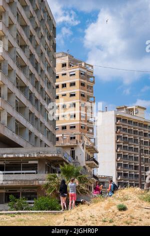 Famagusta, Zypern - 20. April 2022: An einem sonnigen Tag blicken die Menschen auf die verlassenen Hotels am Strand der Geisterstadt Varosha Famagusta. Stockfoto