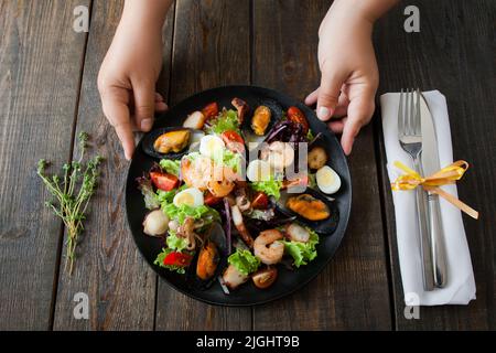 Kellner serviert Gericht mit warmem Seafood-Salat. Kellner-Hände, die einen Salat mit gegrillten Meeresfrüchten auf den Tisch legen, Esser pov Stockfoto