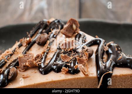 Kakao-Soufflé-Kuchen mit Schokoladensauce und Chips und Kaffeebohnen auf schwarzem Teller auf Holzkloset Stockfoto