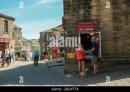 Haworth, West Yorkshire, Großbritannien. Ein Paar, das an einem warmen Sommertag in einem Café in der Main Street Haworth ein Eis von einer Servierluke kauft. Stockfoto