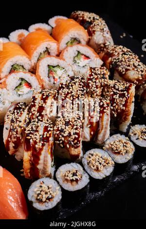 Nahaufnahme eines großen Sets verschiedener Sushi-Brötchen mit verschiedenen frischen Fisch- und Gemüsefüllungen, die auf einem schwarzen Teller serviert werden. Traditionelle japanische Küche. M Stockfoto