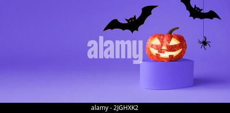 Halloween-Party-Konzept. Kürbis auf dem Podium und schwarze Fledermäuse auf violettem Hintergrund. Halloween Weihnachtsschmuck. Stockfoto