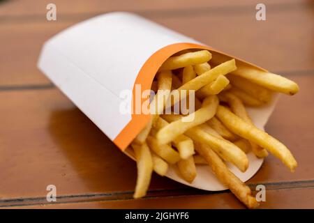 Eine Tüte goldener Pommes Frites liegt auf dem Tisch eines Cafés im Freien. Stockfoto