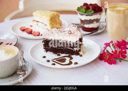 Natürliche vegane, geschichtete Desserts, ein Stück Kuchen mit frischen Früchten und Beeren draußen und ein Glas Latte. Feier, Sortiment von Süßigkeiten auf dem ter Stockfoto