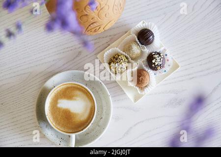 Sortierte, zuckerfreie vegane Trüffel ohne Backen, Mehl und Milch. Tasse Cappuccino auf einem Holztisch im Café. Natürliche Süßigkeiten. Kaffeepause. Lavendel Stockfoto