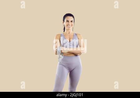Porträt einer freundlichen, starken, sportlichen Fitnesstrainerin mit Maßband in den Händen. Stockfoto