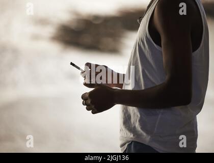 Es ist Zeit, den Ausweg zu nehmen. Ein unkenntlich geworfter Mann, der vor städtischem Hintergrund eine Marihuanazigarette raucht. Stockfoto