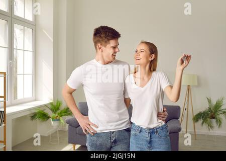 Glückliches junges Paar in der Liebe umarmt in ihrer neuen Wohnung mit den Schlüsseln in den Händen. Stockfoto