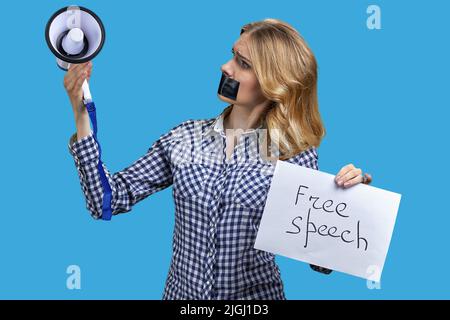 Verärgerte Frau protestierte mit Klebeband über dem Mund und schaute auf Megaphon in ihrer Hand. Freie Meinungsäußerung. Stockfoto