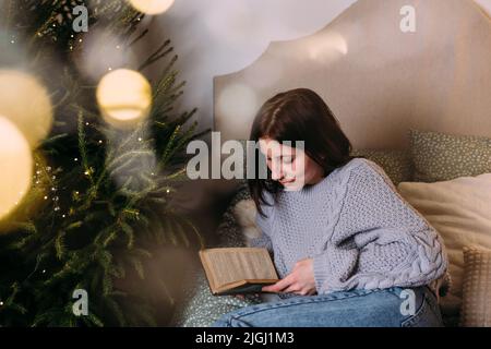 Attraktive Frau liest ein Buch auf dem Bett in gemütlicher Weihnachtsatmosphäre Stockfoto