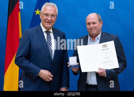 11. Juli 2022, Bayern, MŸnchen: Joachim Herrmann (l, CSU), Bayerischer Innenminister, überreicht die Bayerische Staatsmedaille "Stern der Sicherheit" an Manfred Steger, den ehemaligen Leiter der Notdienstabteilung der AOK Bayern. Mit der Bayerischen Staatsmedaille "Stern der Sicherheit" würdigt der Bayerische Innenminister seit 2013 herausragende Verdienste um die innere Sicherheit. Foto: Sven Hoppe/dpa Stockfoto