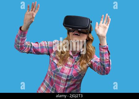 Aufgeregt Mädchen mit Virtual-Reality-Headset auf blauem Hintergrund. Frau verwendet virtuelle Brille. Stockfoto