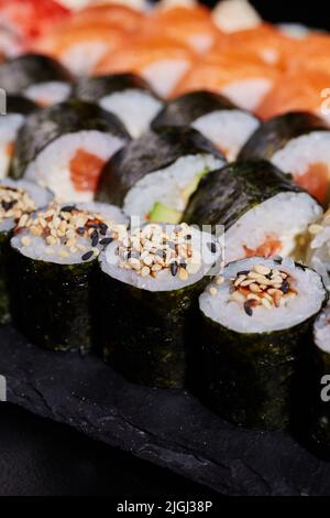 Nahaufnahme von Maki-Sushi mit Sesam, eingewickelt in Nori-Blätter. Unscharfer Hintergrund. Selektiver Fokus. Stockfoto