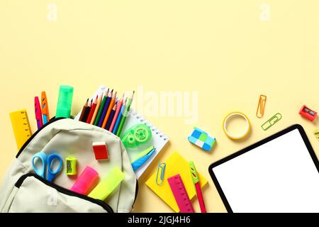 Rucksack mit bunten Schulbedarf auf gelbem Tisch, Draufsicht. Zurück zum Schulkonzept. Stockfoto