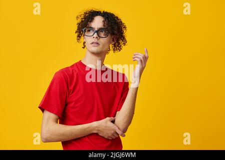 Nachdenklich nachdenkliche myopische junge Student Mann in roten T-Shirt lustige Brille posiert isoliert auf über gelben Studio-Hintergrund. Das beste Angebot mit gratis Stockfoto