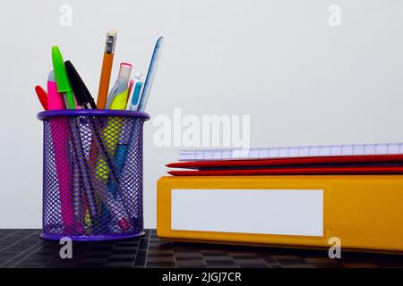 Schulmappen und Schreibwaren auf weißem Hintergrund mit Platz für Kopien. Mehrere Schulmaterialien in einem Stifthalter und Ringordnern mit leerem Etikett organisiert Stockfoto