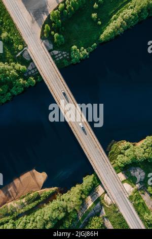 Drone Draufsicht auf leere Autobrücke über wunderschönen dunkelblauen Fluss. Luftbrücke von oben im hellen Sommer. Abendlicht. Erstaunliche Drohne Draufsicht vertikale Aufnahme Stockfoto