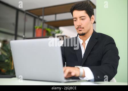 Serious konzentriert bestimmt junge bärtige Büroangestellte in Business Casual Kleidung, sitzen am Schreibtisch, tippen auf Laptop, Geschäftsmann professionell arbeitet an Projekt, E-Mail an den Kunden schreiben Stockfoto