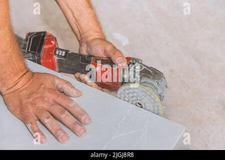Ein Arbeiter poliert die Ecken der geschnittenen Fliesen mit einer Polierscheibe mit Diamant auf einem Winkelschleifer Stockfoto